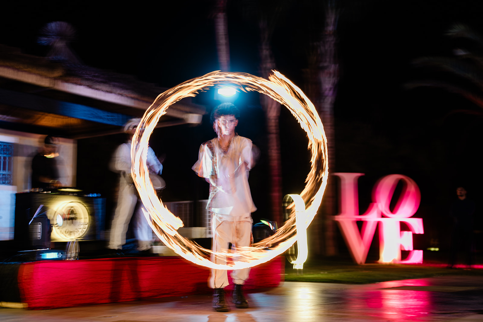 Jongleur de feu réalisant un cercle enflammé devant la sculpture lumineuse LOVE
